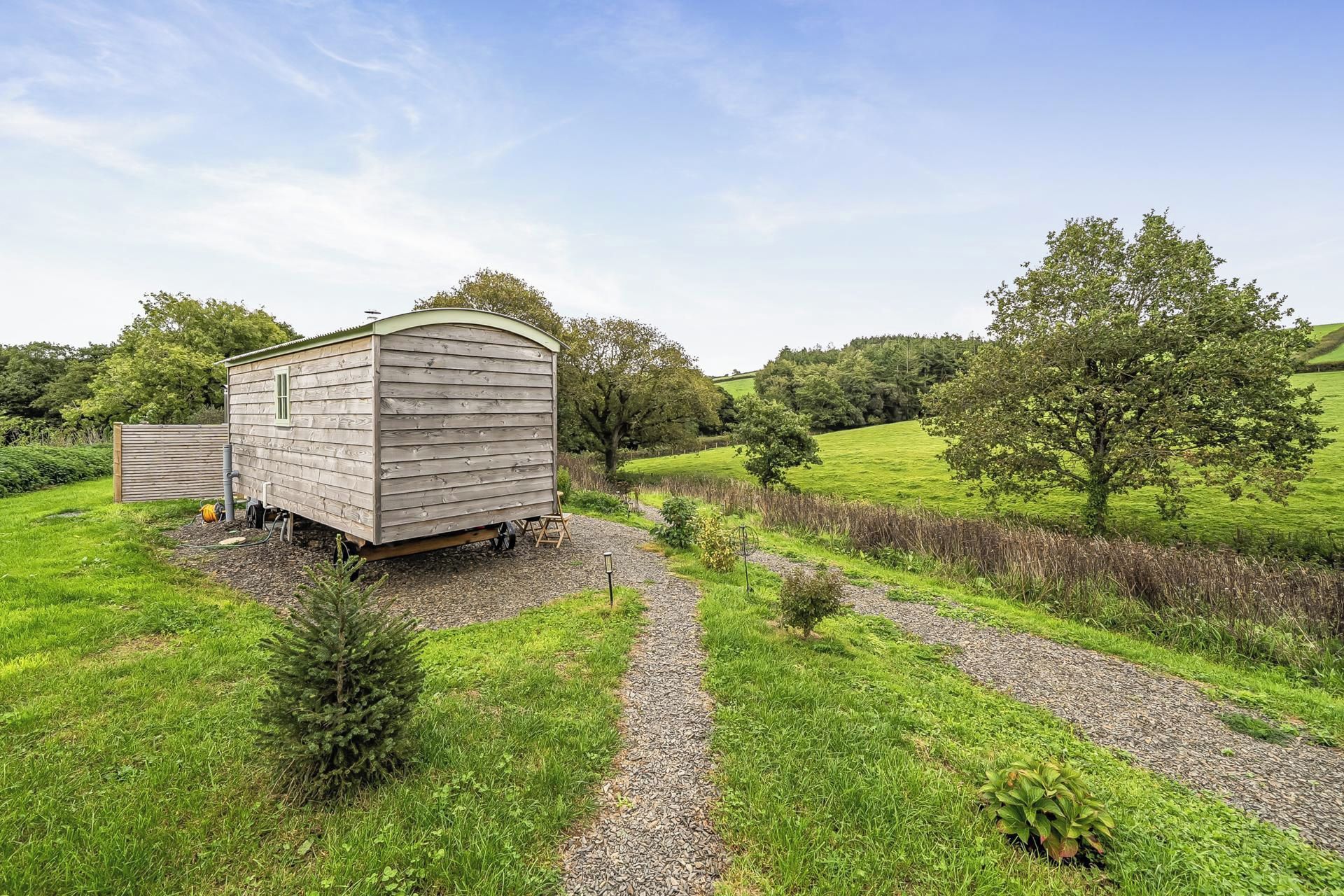 A wooden shed in a rural setting with a gravel path leading to it.