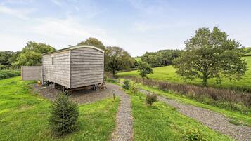 A wooden shed in a rural setting with a gravel path leading to it.