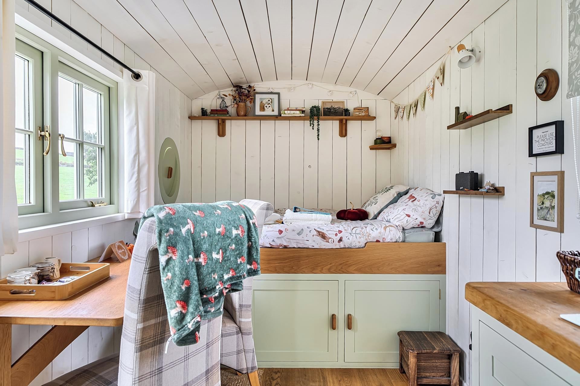 A cozy room with a bed, a small table, a bench, and a window with curtains.