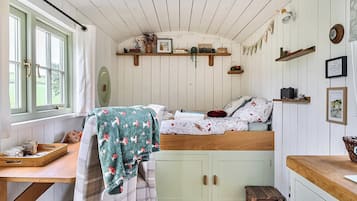 A cozy room with a bed, a small table, a bench, and a window with curtains.