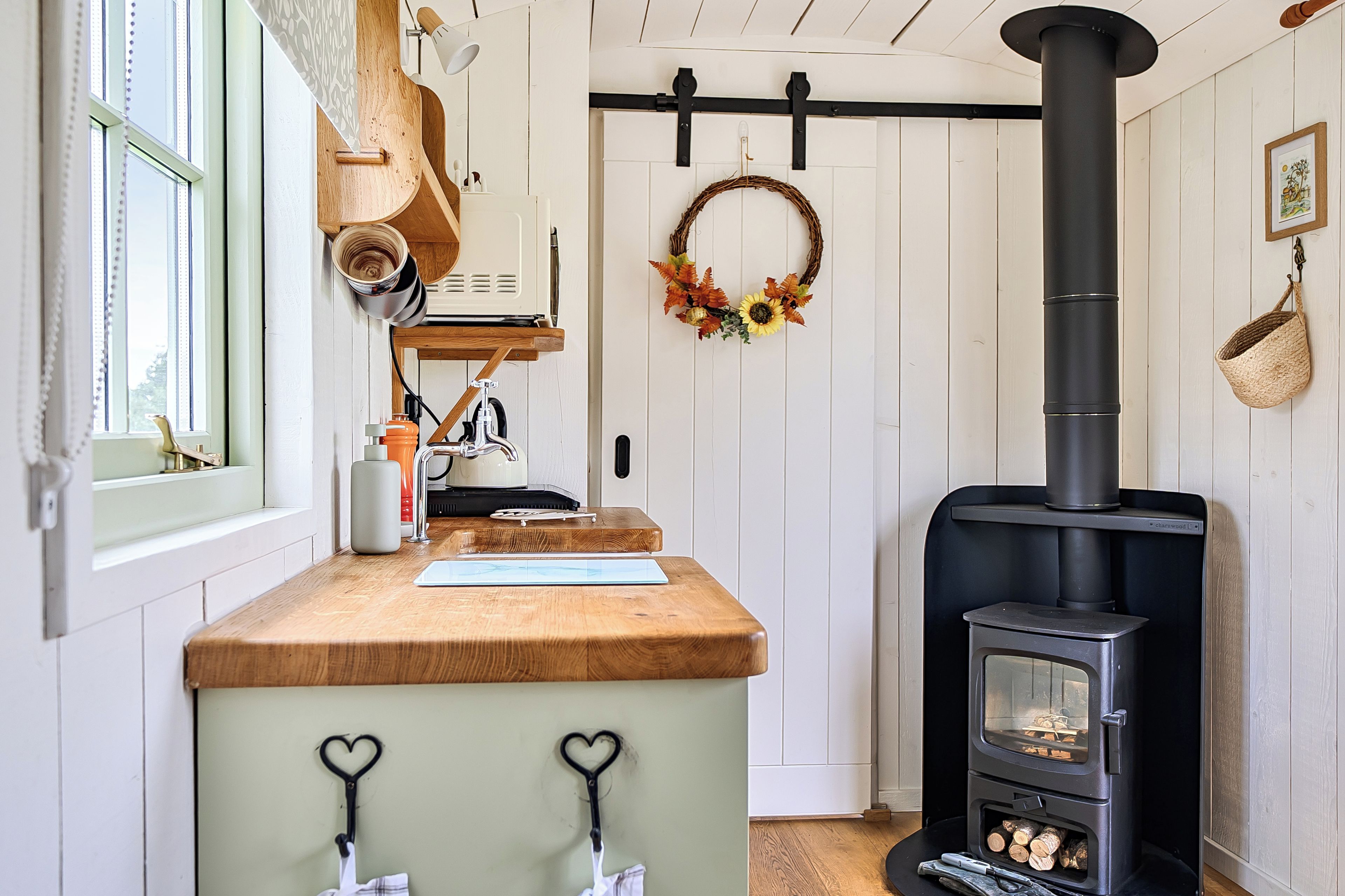 A kitchen with a wood-burning stove, a wooden countertop, and a hanging wreath.