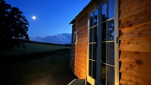 Une cabane en bois dotée de grandes fenêtres, d’une porte et d’un petit espace porche.