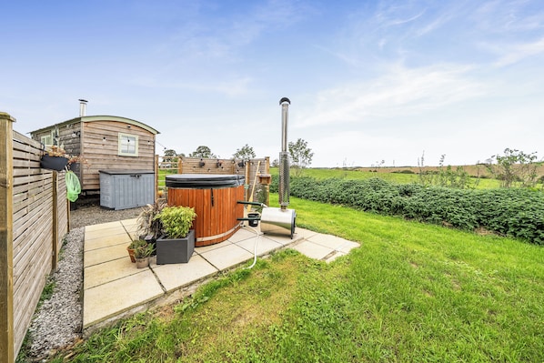 A wooden cabin with a hot tub, a barbecue grill, and a garden area with a lawn and hedges.