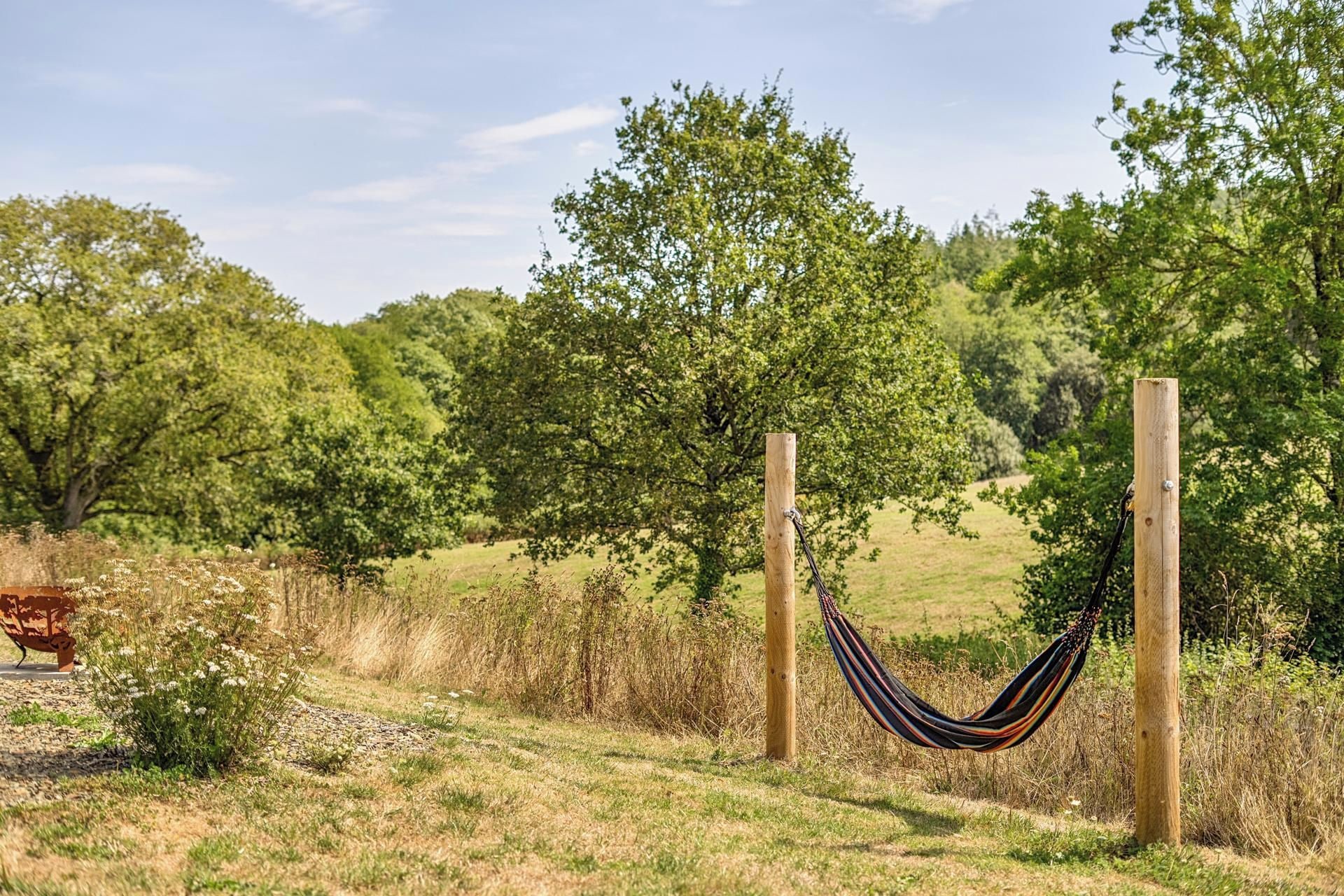 A hammock tied between two wooden posts in a grassy field with trees in the background.