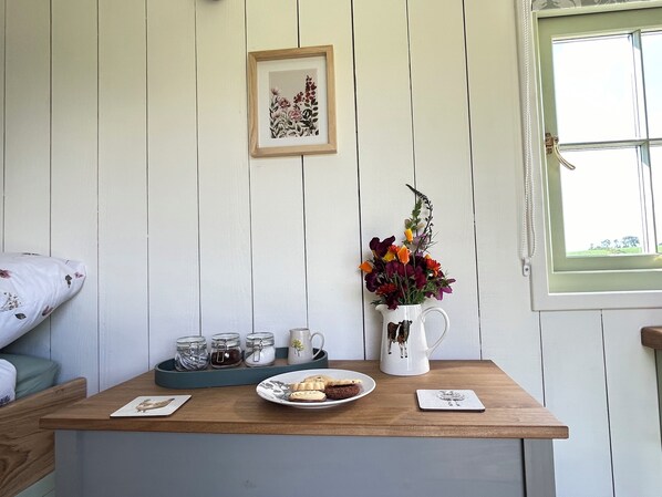 A wooden table with a tray holding a plate of cookies, a pitcher of flowers, and a framed picture on the wall. - Cosy Luxury Foxglove Hut With Private Fire Bowl (Umberleigh)