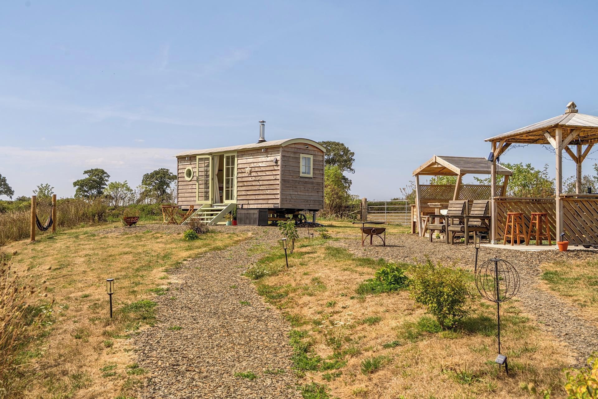 Une cabane en bois rustique, dotée d’une véranda, d’un petit abri de jardin et d’un espace salon extérieur.