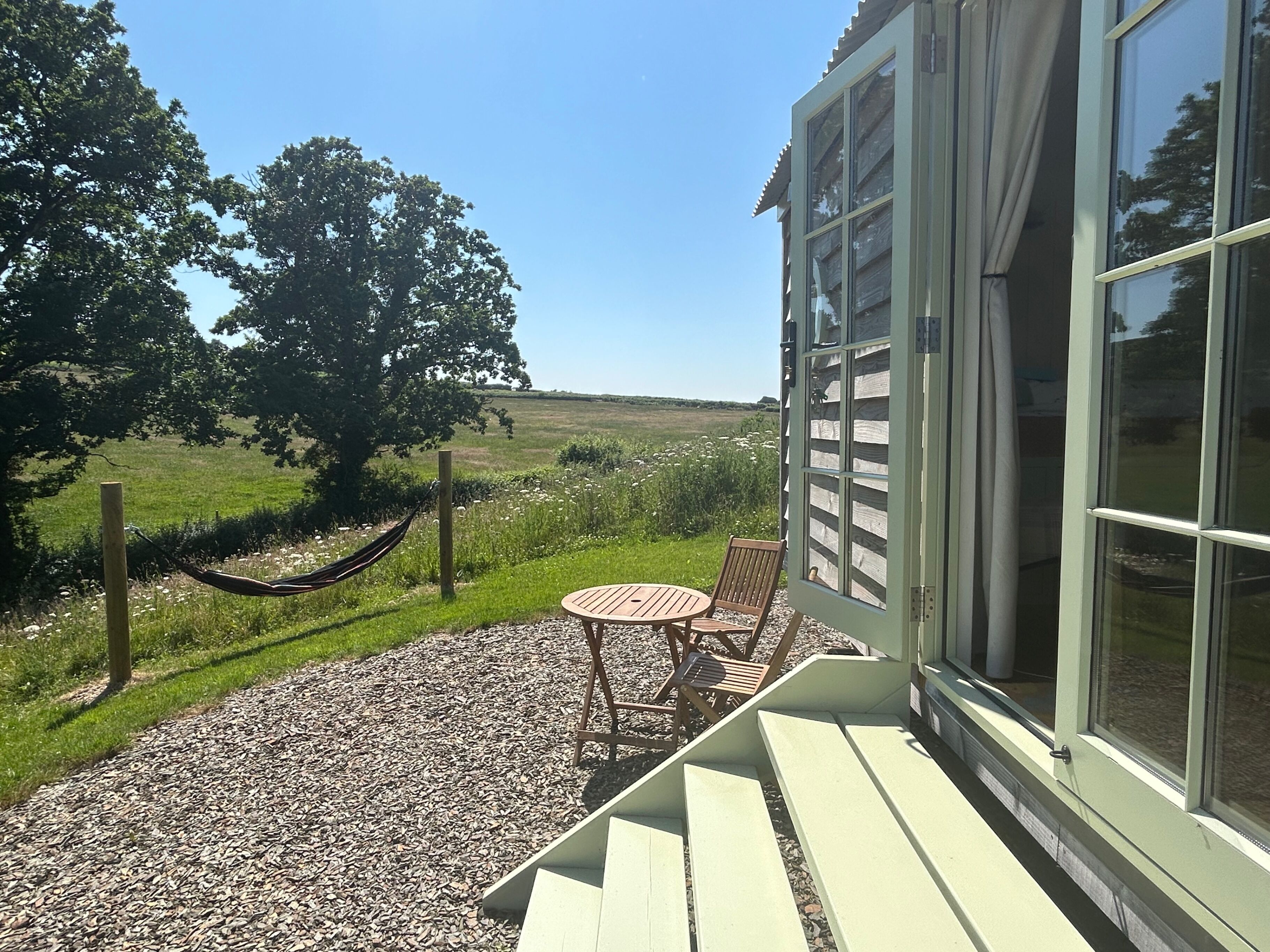 Un patio con una mesa y sillas, una hamaca y vistas a un campo cubierto de hierba.