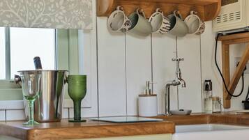 A kitchen with a wooden countertop, a hanging pot rack, and a window with a patterned curtain.
