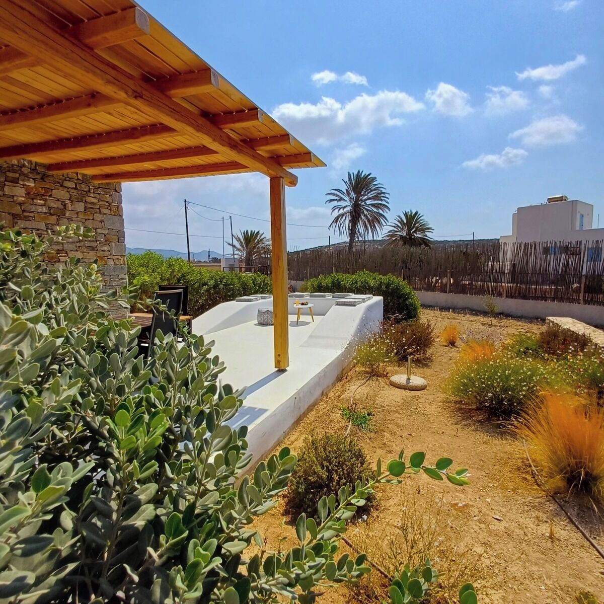 Un patio con muro de piedra, pérgola de madera y una zona de estar.