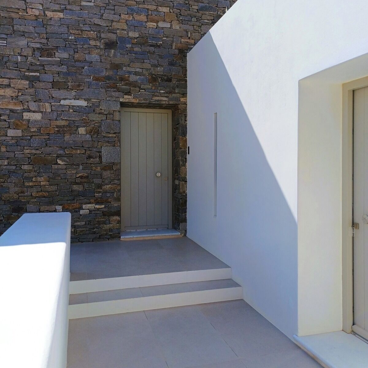 Un edificio moderno con fachada de piedra, una puerta gris y una pared exterior blanca.