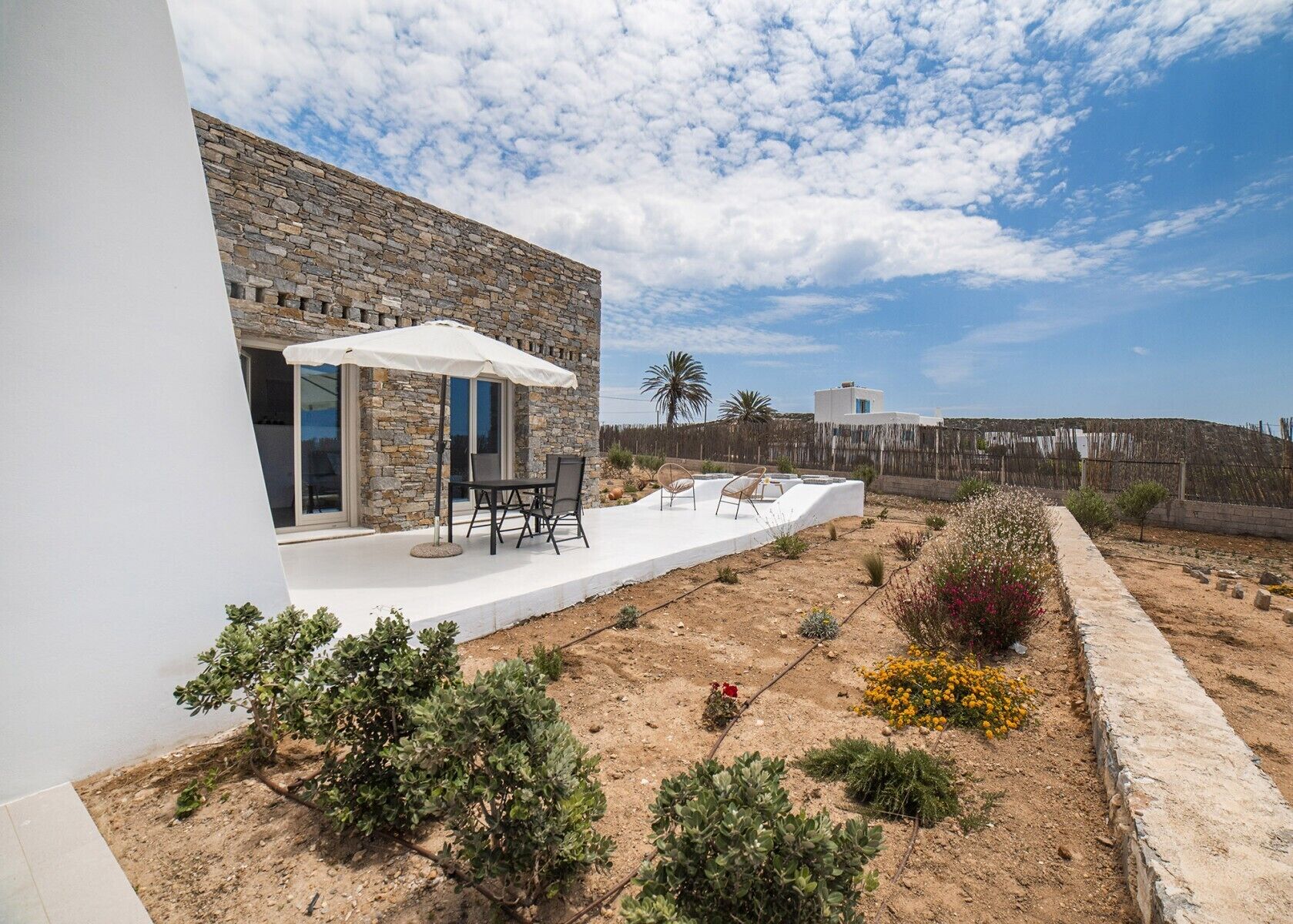 Une maison moderne avec une façade en pierre, un patio doté de mobilier d’extérieur et une vue sur le paysage environnant.