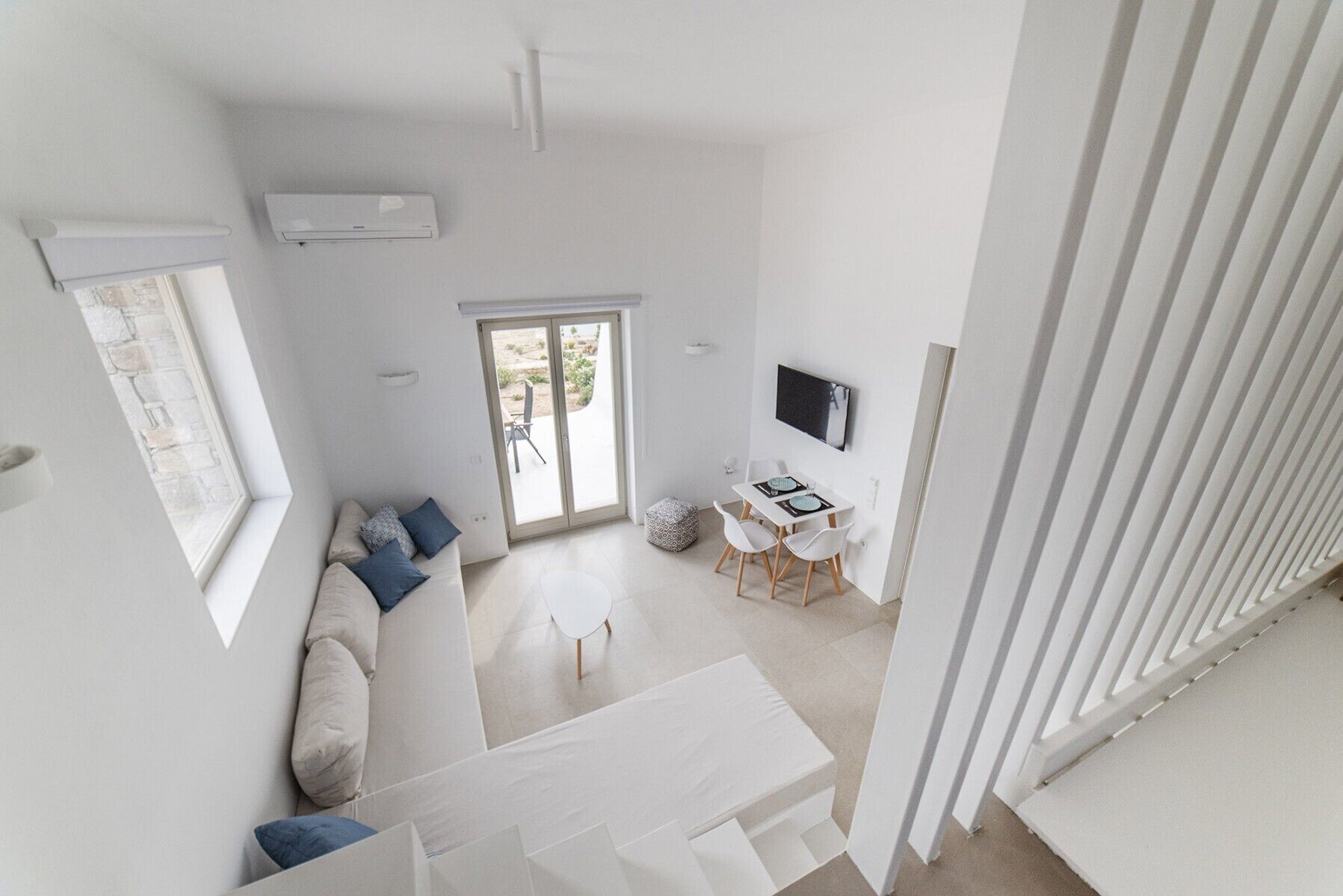 A modern, open-plan living space with a sofa, dining table, and a view through a sliding door to an outdoor area.