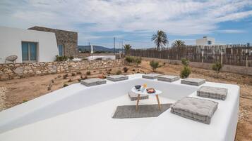Un espace extérieur moderne, aménagé avec des murs en pierre, une table blanche et des coussins.