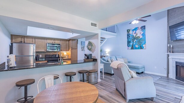 Eine moderne Küche mit Kochinsel, ein Essbereich mit rundem Tisch und ein Wohnzimmer mit Sofa und Kamin.