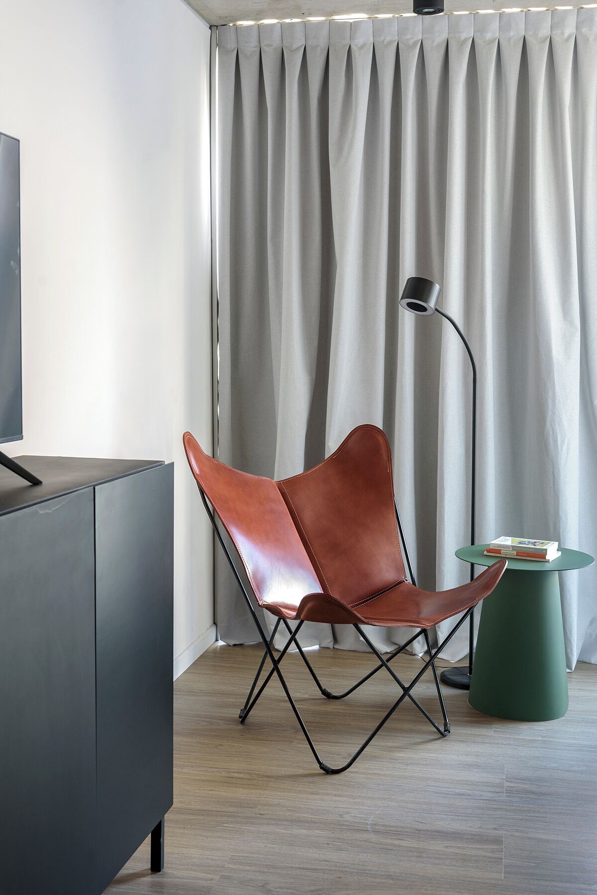 Una habitación moderna con un sillón de cuero, una mesita, una lámpara de pie y un televisor sobre un mueble.