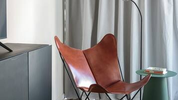 Una habitación moderna con un sillón de cuero, una mesita, una lámpara de pie y un televisor sobre un mueble.