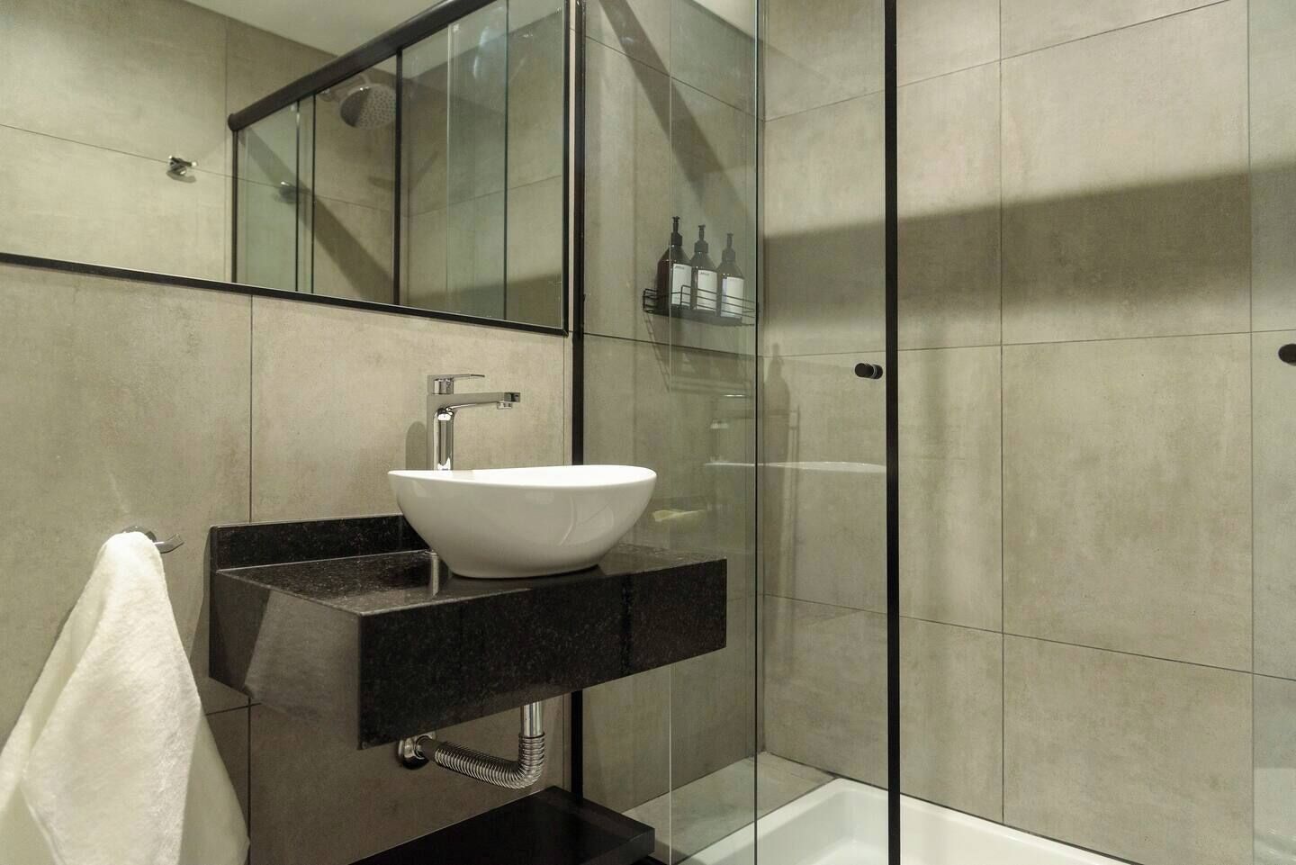 Ein modernes Badezimmer mit einem weißen Aufsatzwaschbecken, einer schwarzen Arbeitsplatte, einer Duschkabine aus Glas und einem sichtbaren Handtuchhalter.