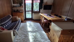 A cozy room with a sofa, a fluffy rug, a wooden table, and a window with a view of trees. - Wuthering Heights Apartment, lovely apartment at the foot of the ski slopes (Angolo Terme)