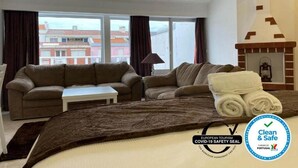 Una habitación de hotel con dos sofás, una mesita, una chimenea y vistas a edificios.