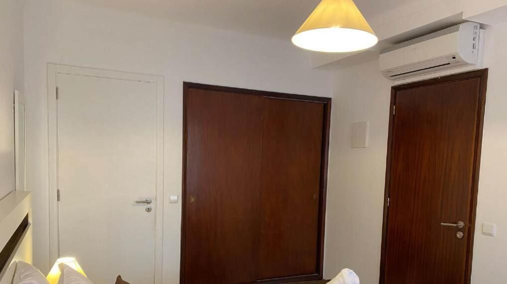 A hotel room with two wooden doors, a ceiling-mounted air conditioning unit, and a hanging light fixture.
