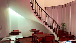 Un vestíbulo de hotel con una escalera curva, suelo de madera y mesas con sillas.