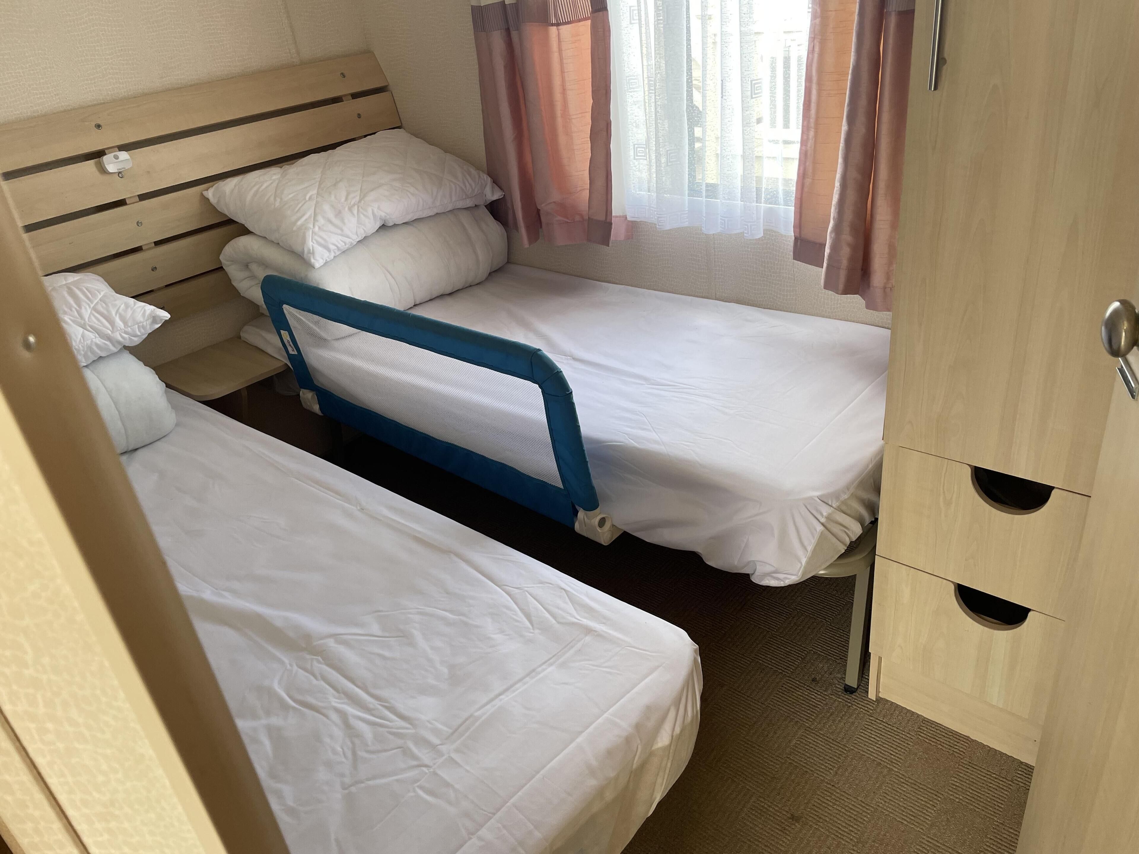 A compact bedroom with two single beds, a wooden headboard, a small table, and a wardrobe with a mirror.