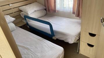 A compact bedroom with two single beds, a wooden headboard, a small table, and a wardrobe with a mirror.