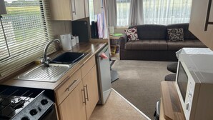 Cocina compacta con estufa, lavaplatos y microondas.  Cuenta con un pequeño comedor con mesa y sofá.