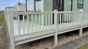 Una casa móvil verde con un porche cubierto y una terraza blanca.