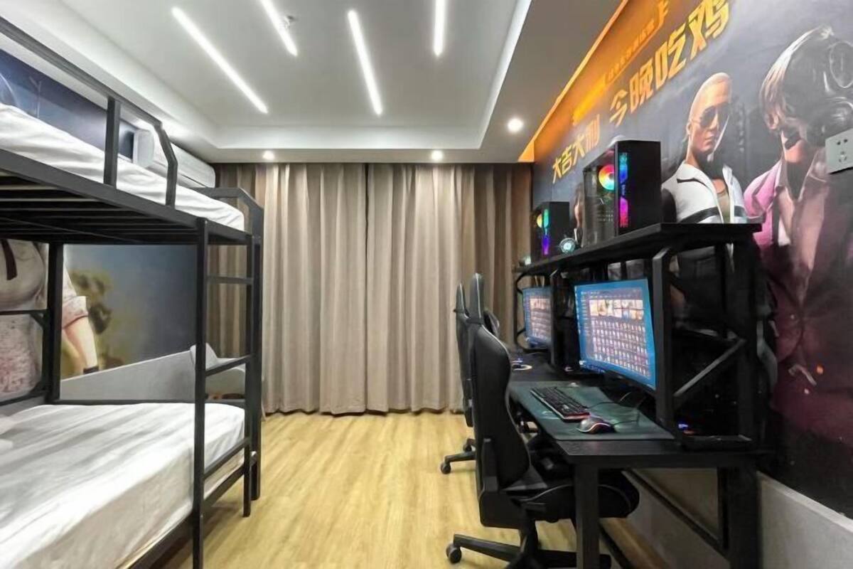 Una habitación con literas, un escritorio con dos monitores y una configuración para videojuegos.