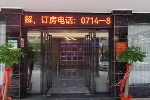 Entrada de un hotel con puerta de cristal, mostrador de recepción y un número de teléfono visible en la parte superior.