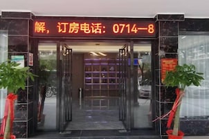 Entrada de un hotel con puerta de cristal, mostrador de recepción y un número de teléfono visible en la parte superior.