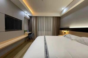 Una camera d'albergo moderna con un letto grande, una scrivania con sedia, una TV a schermo piatto montata a parete e un comodino con lampada.