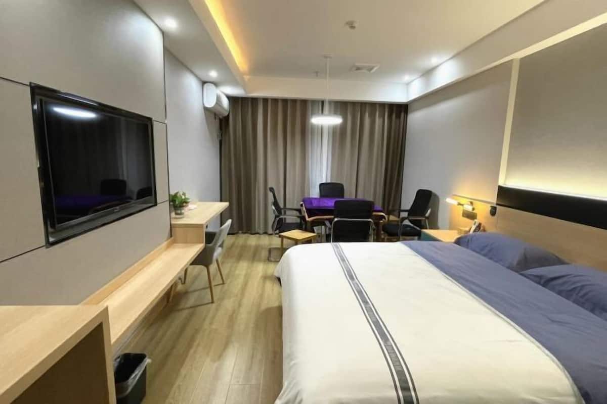 Una habitación de hotel con cama, escritorio, silla, televisión y cortina.