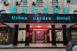 La entrada del Urban Garden Hotel, con un letrero destacado, una puerta roja y una estatua en el vestíbulo.