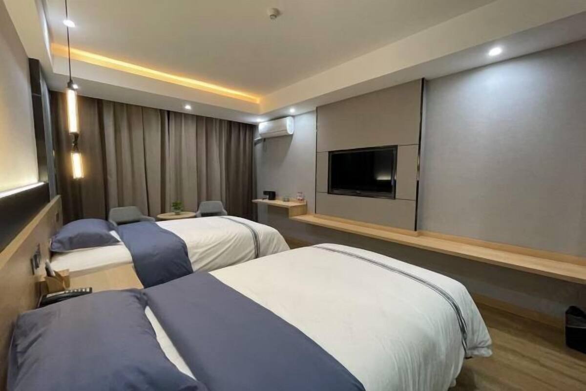 Una habitación de hotel moderna con dos camas, una televisión de pantalla plana, un escritorio y un aire acondicionado instalado en la pared.