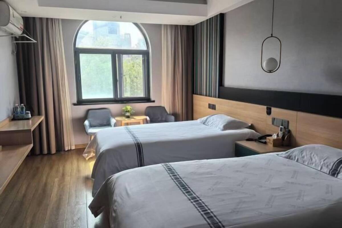 Habitación de hotel con dos camas, un escritorio, una silla, un ventanal y una mesita con una planta.
