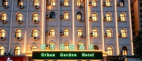 A multi-story hotel with a symmetrical facade, arched windows, and a sign reading 'Urban Garden Hotel.'