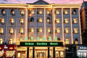 Un hotel de varios pisos con una fachada simétrica, ventanas en arco y un letrero que dice 'Urban Garden Hotel'.