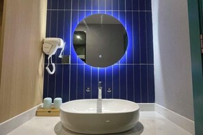 Een badkamer met een ronde spiegel, een witte wastafel en een haardroger op een wandhouder.