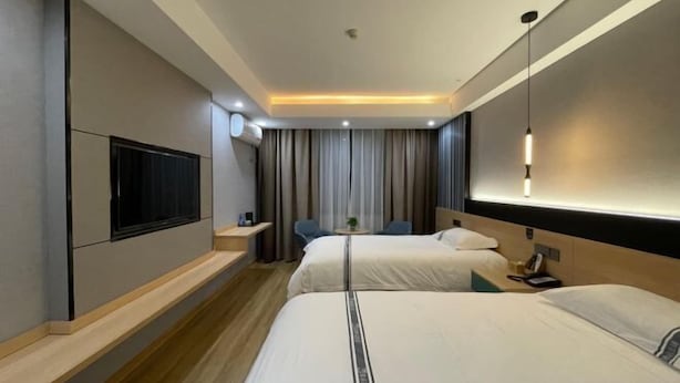 Une chambre d’hôtel moderne équipée de deux lits, d’un téléviseur fixé au mur, d’un bureau avec une chaise et d’une petite table agrémentée d’une plante.