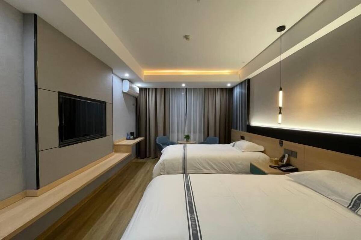 Una habitación de hotel moderna con dos camas, un televisor montado en la pared, un escritorio con una silla y una mesita con una planta.