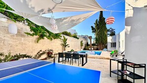 A courtyard with a ping pong table, outdoor seating, a pool, and a white building.