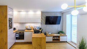 Una cocina moderna con armarios blancos, encimera de madera, horno empotrado y televisor montado en la pared.