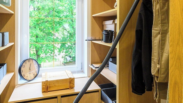 Un armario compacto y bien organizado con estantes de madera, una ventana con vistas a la vegetación y una aspiradora.