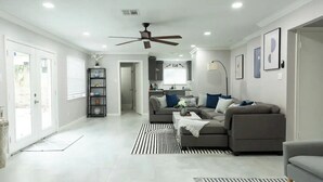 Un salon moderne avec un canapé d’angle gris, un tapis rayé noir et blanc et un ventilateur de plafond.