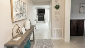 Un couloir moderne avec une cheminée, une enseigne portant le mot « MAISON » et, au fond, un coin repas.