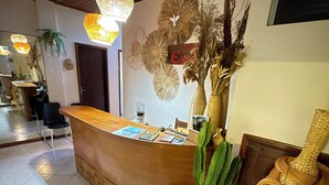 A reception area with a curved wooden counter, a large potted plant, and decorative wall art. - Pousada Estevão (Cairu)