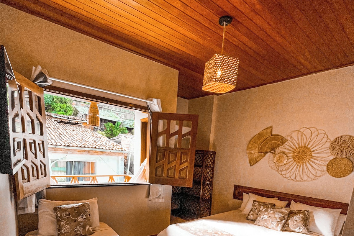 Une chambre d’hôtel avec deux lits, une fenêtre donnant sur des immeubles, un plafond en bois et un mur orné d’œuvres d’art décoratives.
