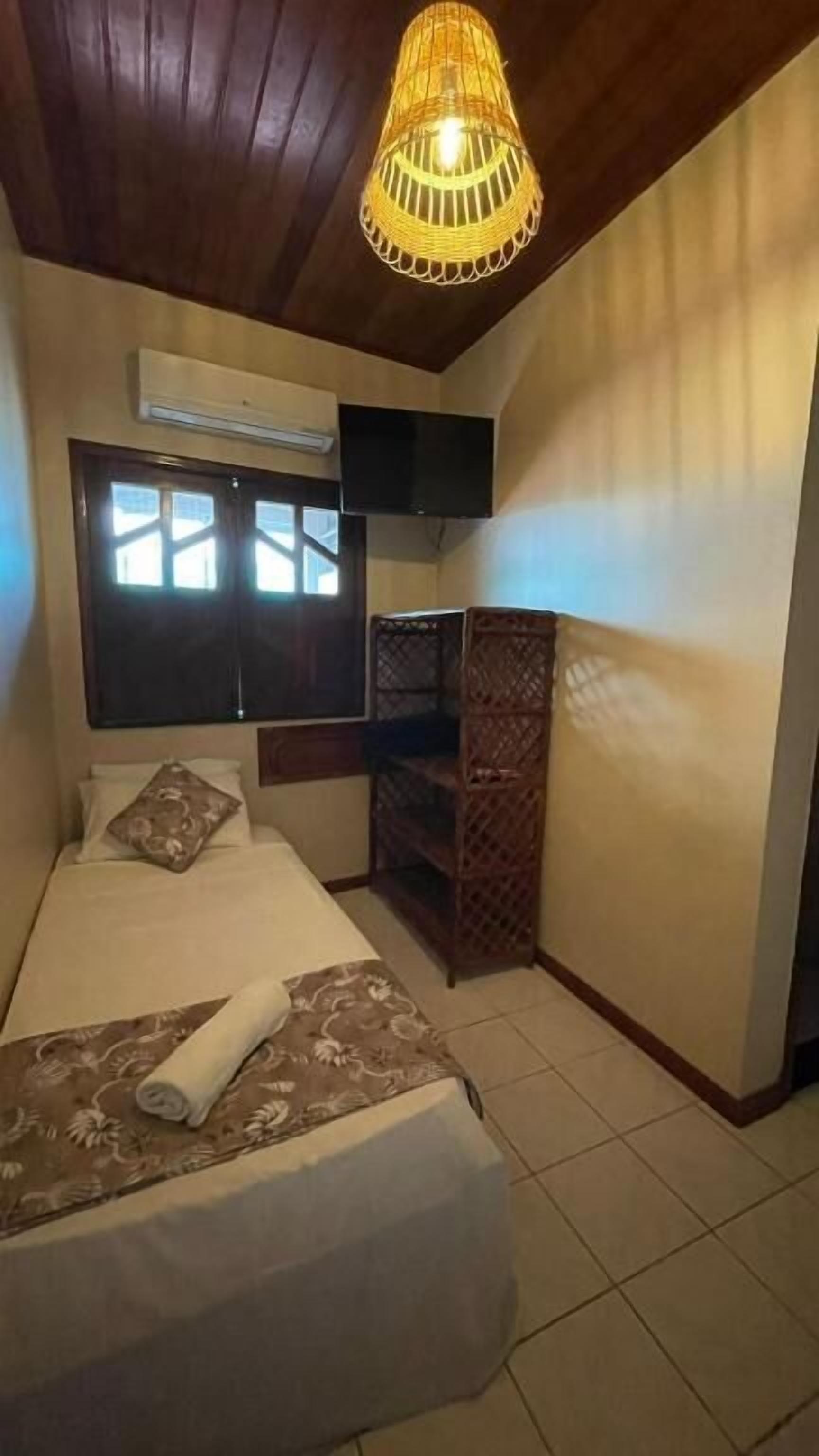 A bedroom with a bed, a television mounted on the wall, a window with blinds, and a ceiling light fixture.